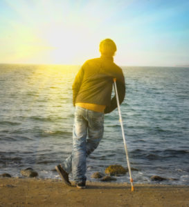 man leaning on a crutch looking out at the ocean