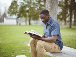 A young man sitting on a park bench reading the Bible