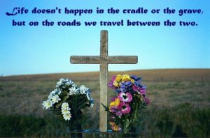 A roadside cross with two bundles of colorful flowers